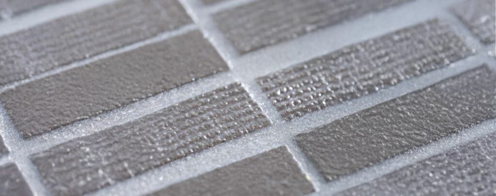 Širokoúhlý pohled na strukturované šedé keramické obklady s lesklými spárami, zvýrazňující jejich reliéfní povrch.