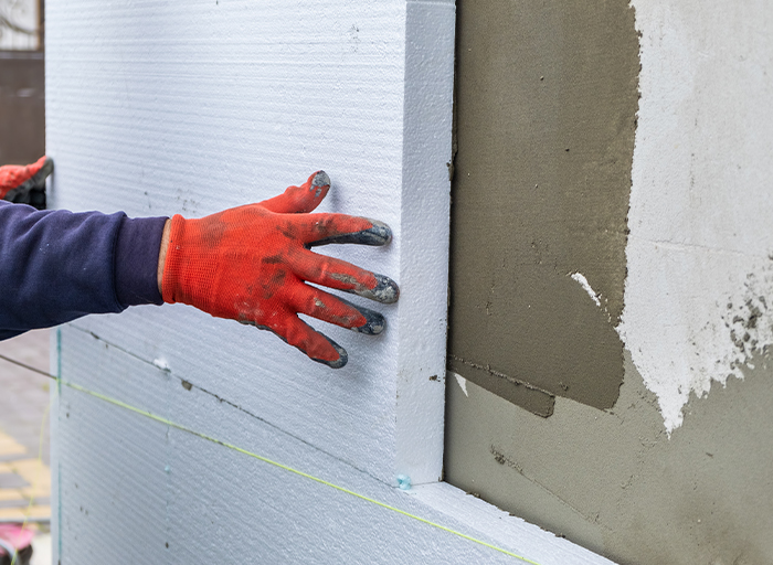 Pracovník přikládá izolační desku na stěnu, příprava pro aplikaci lepidla a perlinky.