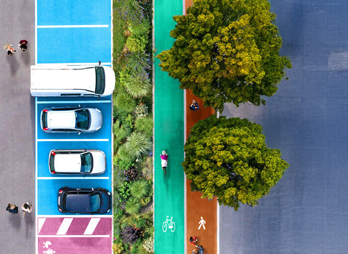 Letecký pohled na barevně rozlišenou cyklostezku a chodník vedle parkovacích míst.